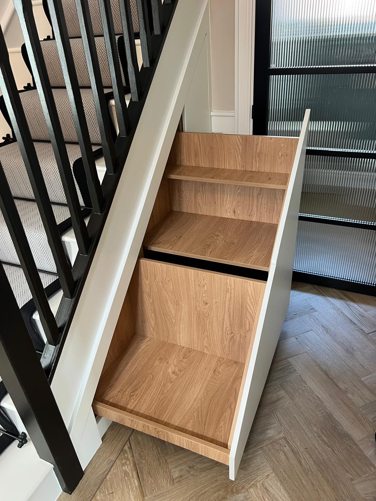 Bespoke pull-out under-stairs storage unit with oak-lined shelves and painted outer panel