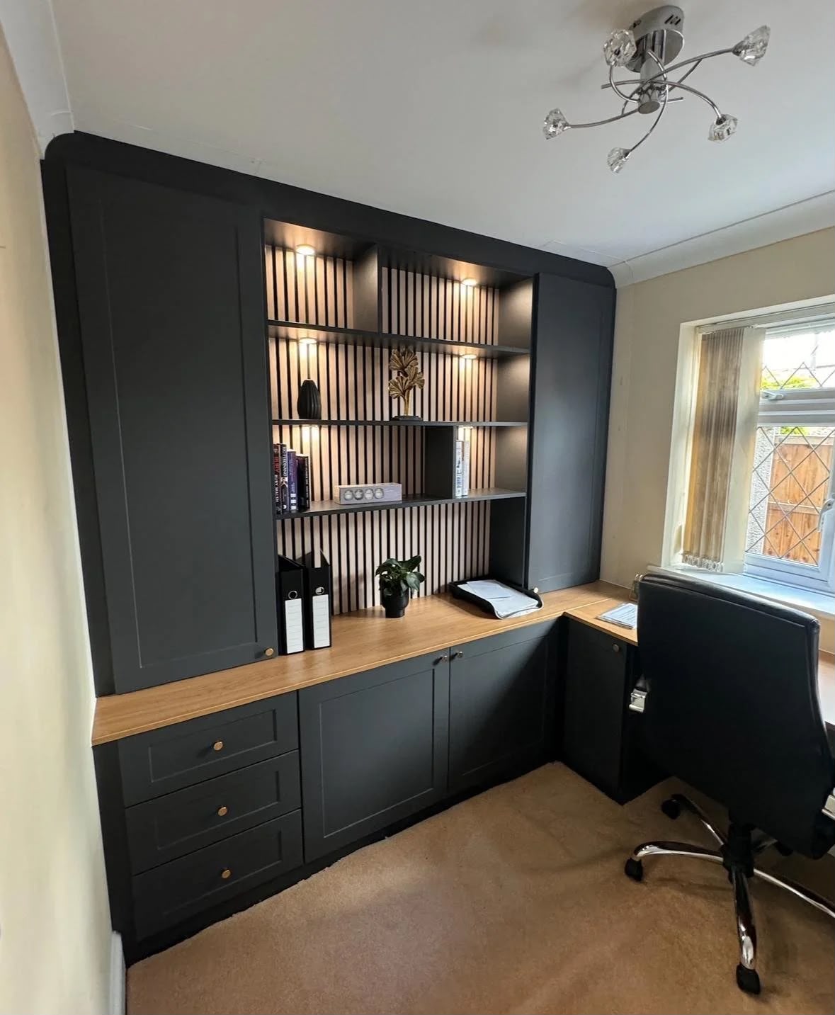 Bespoke home office with dark fitted cabinetry, oak desk top and lit slatted shelving alcove