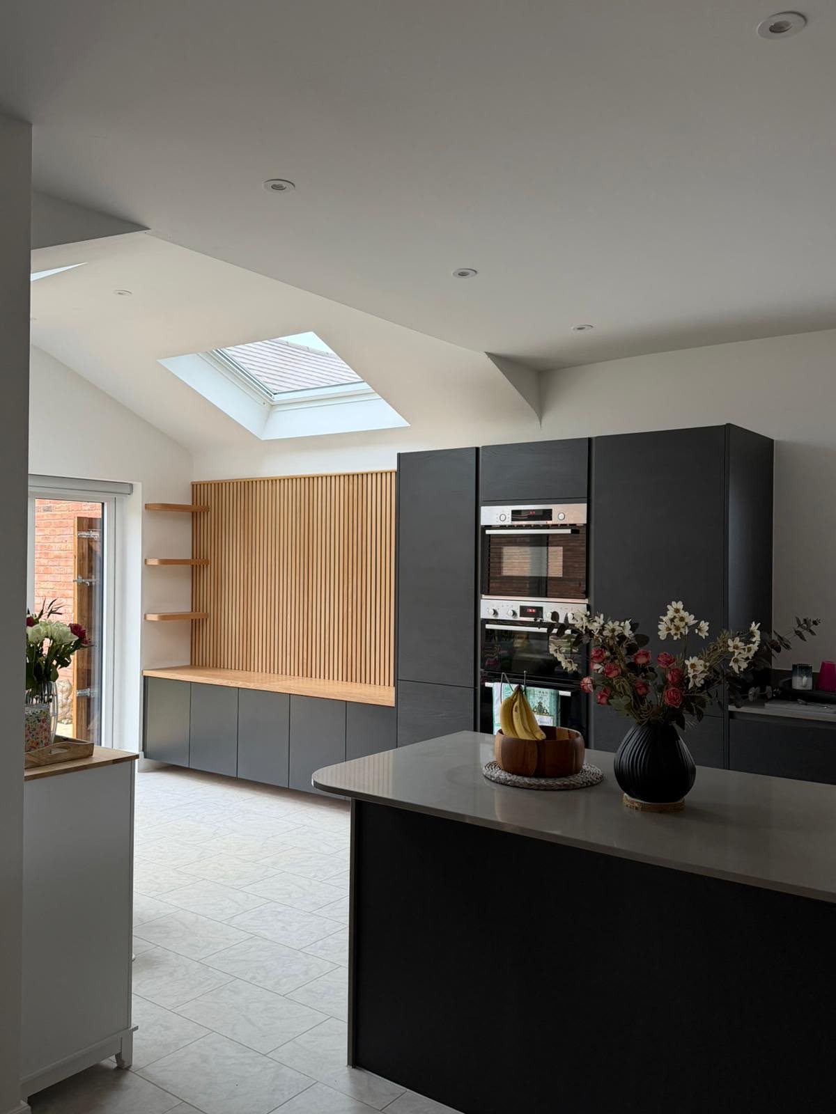 Contemporary dark bespoke kitchen with black cabinetry, integrated appliances and oak slatted timber walls